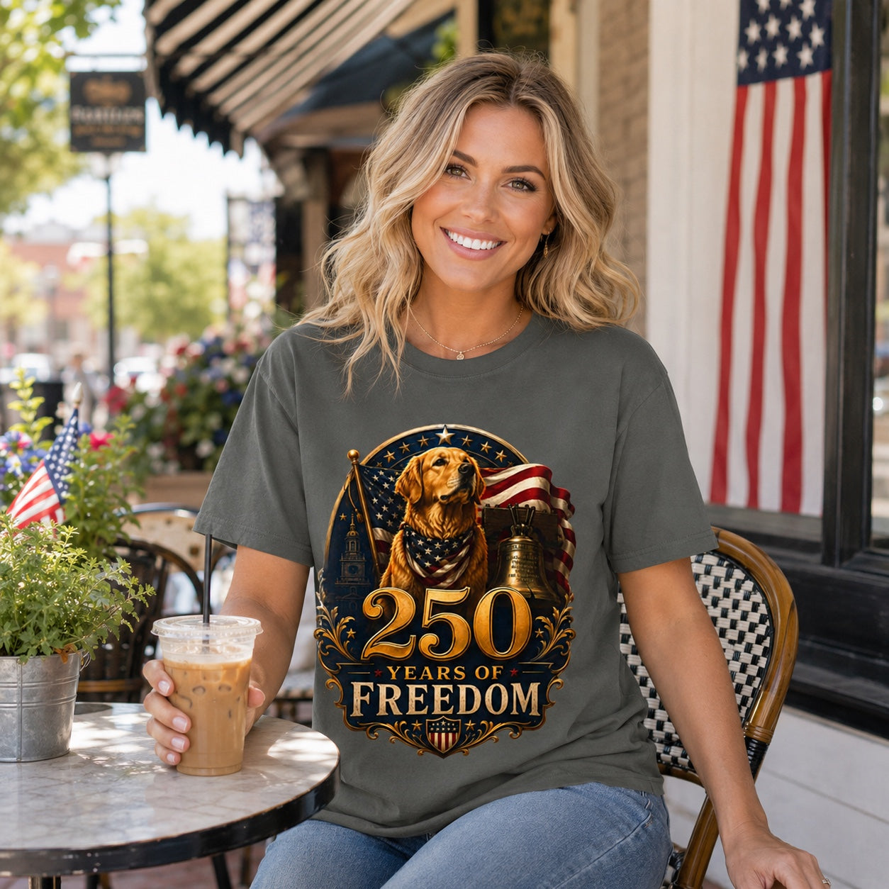 Woman sitting at an outdoor cafe with iced coffee, wearing pepper '250 Years of Freedom' t-shirt