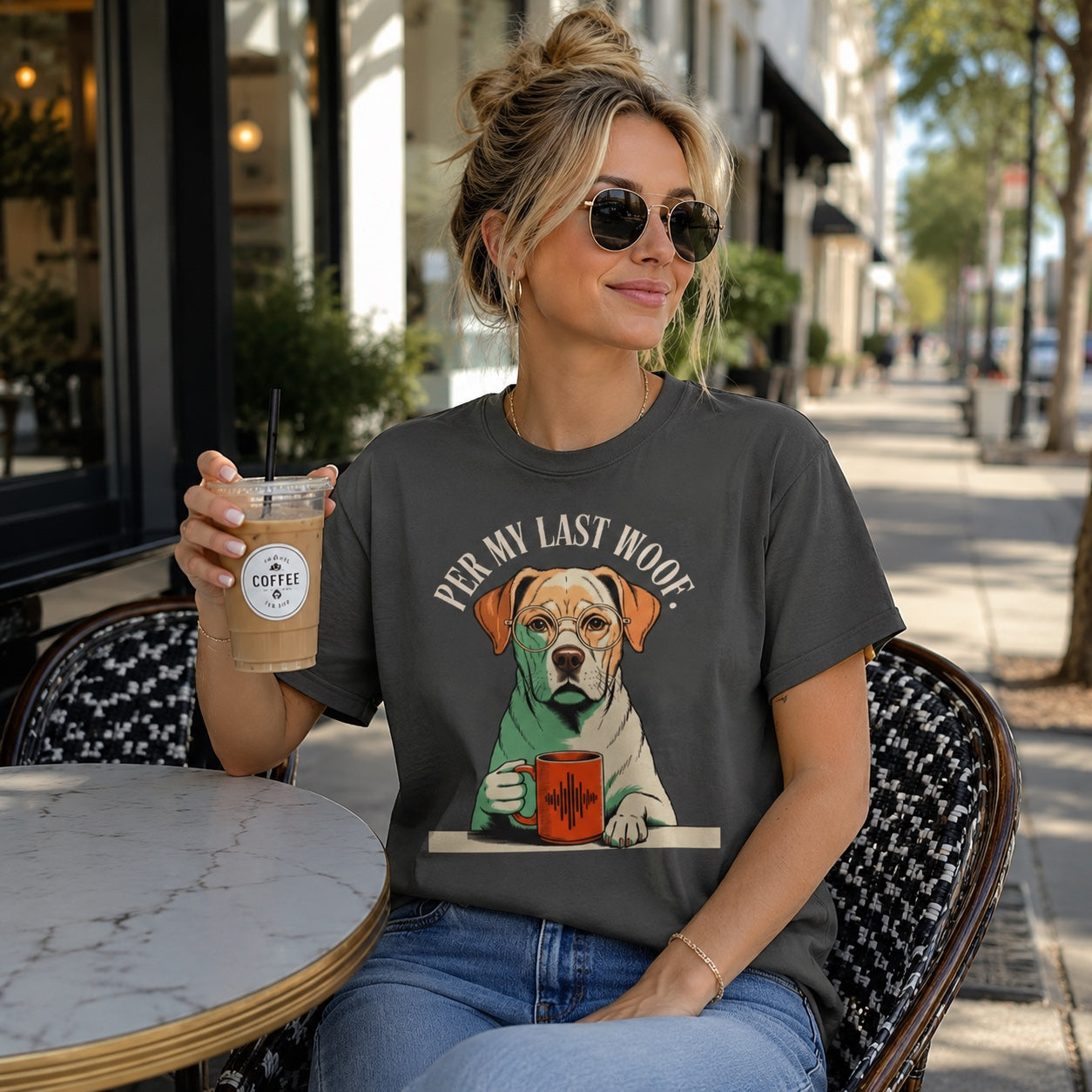 Woman sitting at an outdoor coffee shop table, wearing pepper 'Per My Last Woof' colorful Labrador t-shirt
