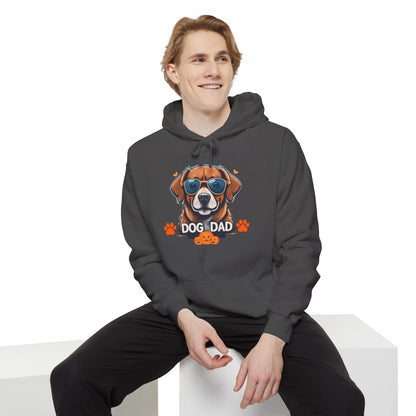 Man sitting while wearing a pepper unisex “Dog Dad” hoodie featuring vibrant sunglasses dog artwork, trendy pet lover hoodie with casual modern fashion style.
