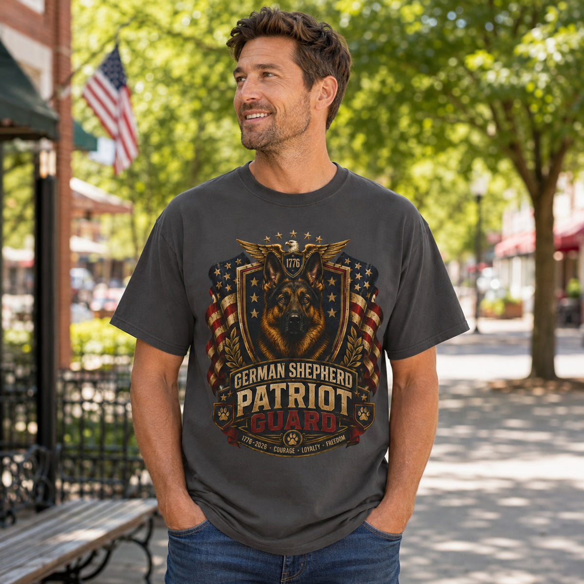Man wearing a graphite German Shepherd Patriot Guard T-shirt with a German Shepherd patriotic crest design in an outdoor town street scene.