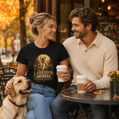Couple drinking coffee at an outdoor café with the woman wearing the black Labrador Coffee Walk Club T-shirt and a Labrador dog beside them.