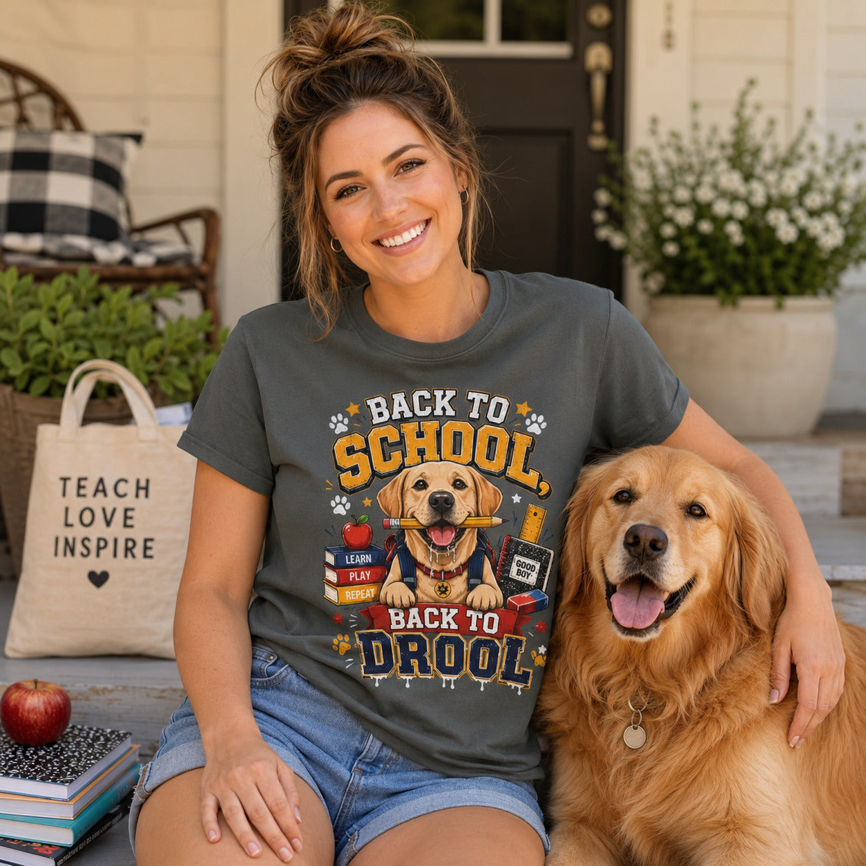 Woman sitting with a 'Teach Love Inspire' tote bag, apple, and books beside her golden retriever, wearing pepper back to school dog t-shirt