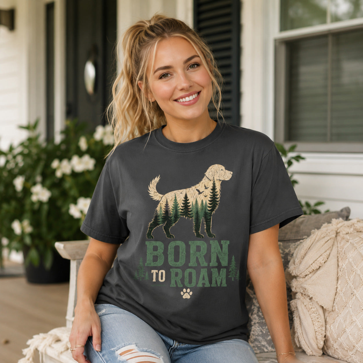 Woman sitting on a porch surrounded by flowers, wearing graphite 'Born to Roam' dog t-shirt
