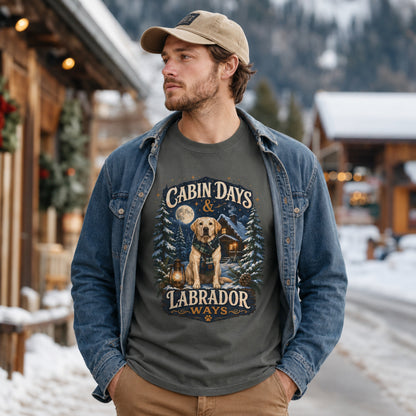 Man wearing a pepper Cabin Days & Labrador Ways T-shirt with a Labrador design in a snowy cabin town street scene.