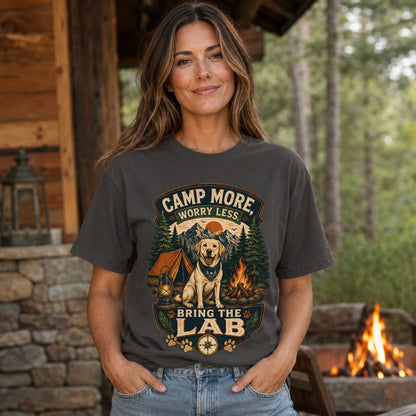 Woman wearing a graphite Camp More Worry Less Bring The Lab T-shirt near a cabin campfire with the Labrador camping artwork clearly visible.