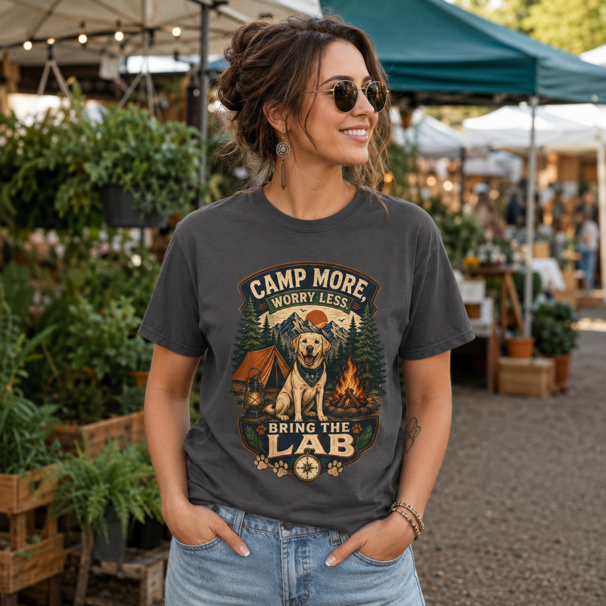 Woman wearing a graphite Camp More Worry Less Bring The Lab T-shirt at an outdoor market with the Labrador camping artwork centered on the chest.