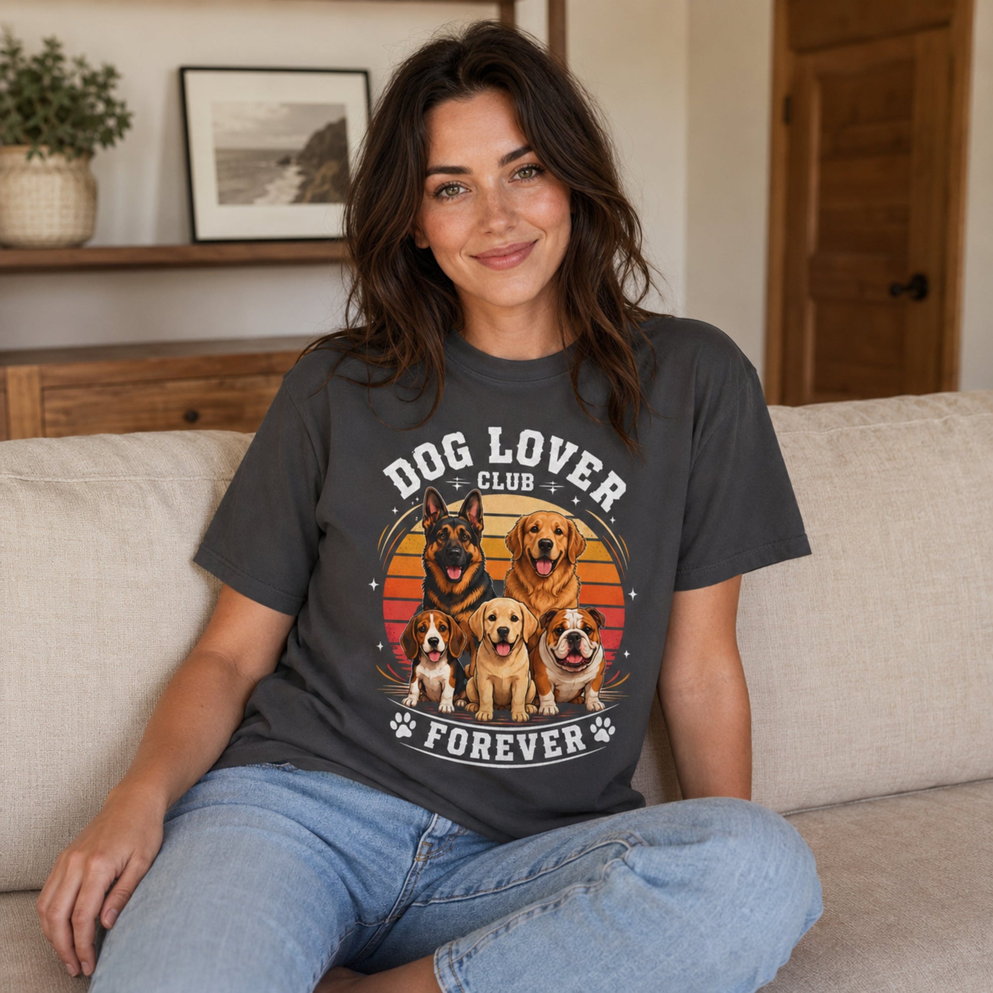 Woman wearing a graphite Dog Lover Club Forever T-shirt with multi-breed dog artwork while sitting on a sofa at home