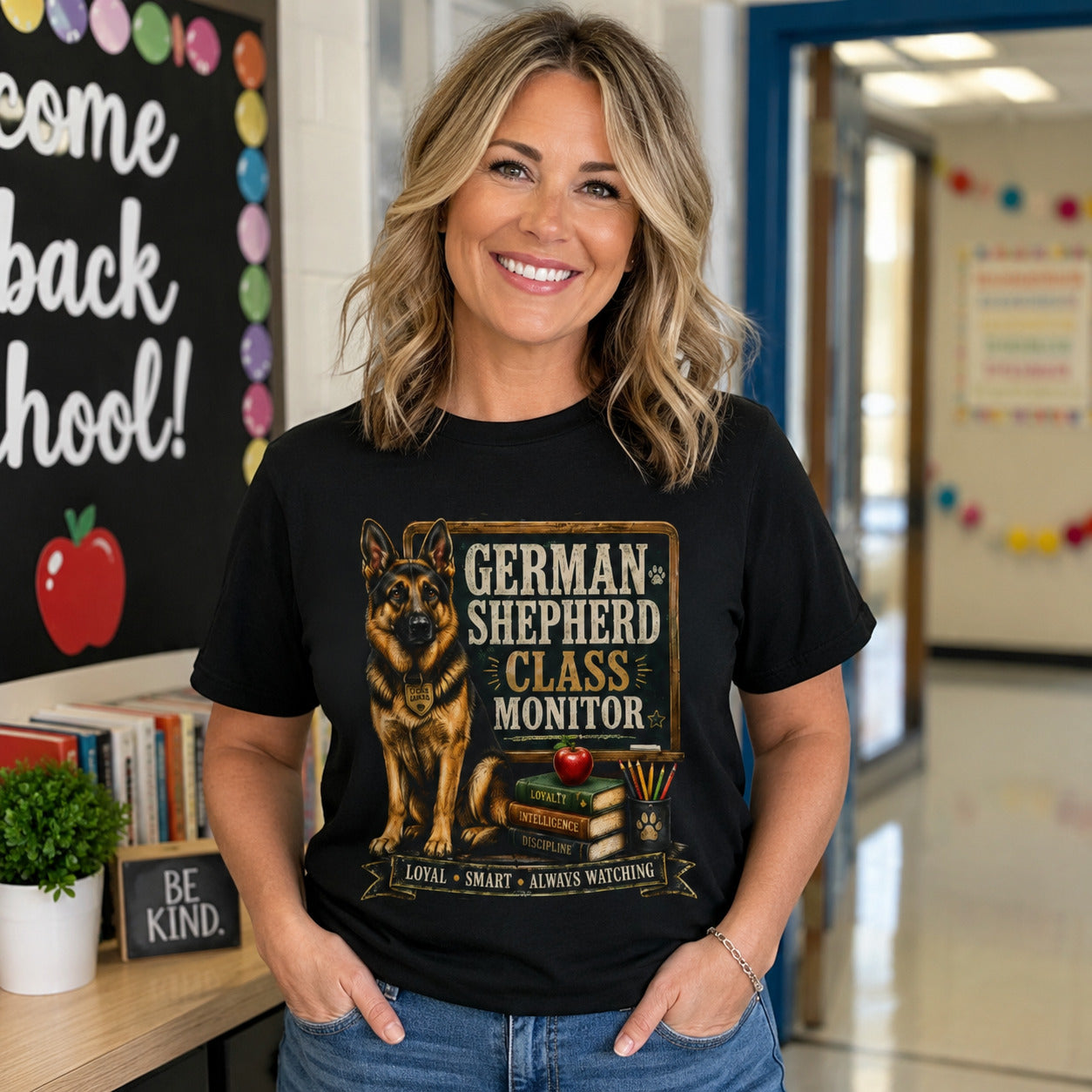 Woman standing in a school hallway near a 'Welcome Back to School' sign, wearing black 'German Shepherd Class Monitor' t-shirt