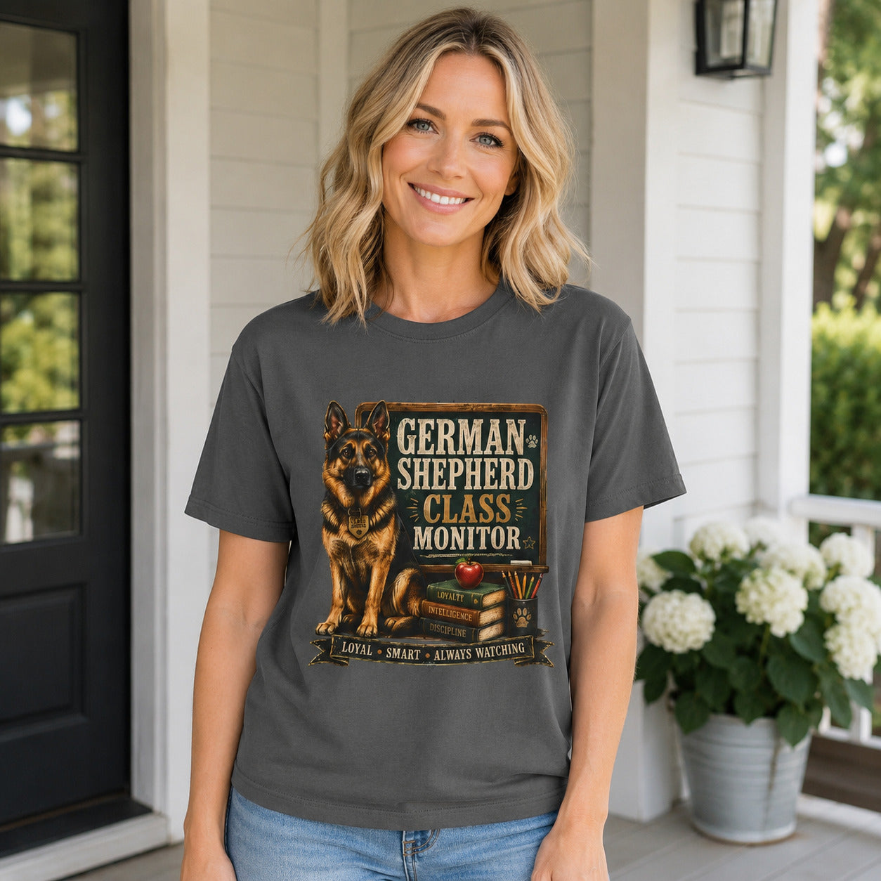Woman standing on a porch surrounded by flowers, wearing pepper 'German Shepherd Class Monitor' t-shirt