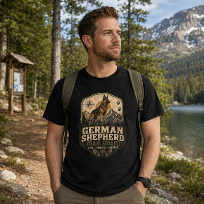 Man wearing a black German Shepherd Trail Guard T-shirt on a lakeside hiking trail.