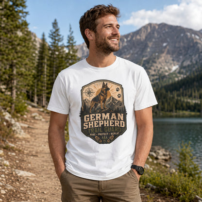 Man wearing a white German Shepherd Trail Guard T-shirt on a lakeside hiking trail.
