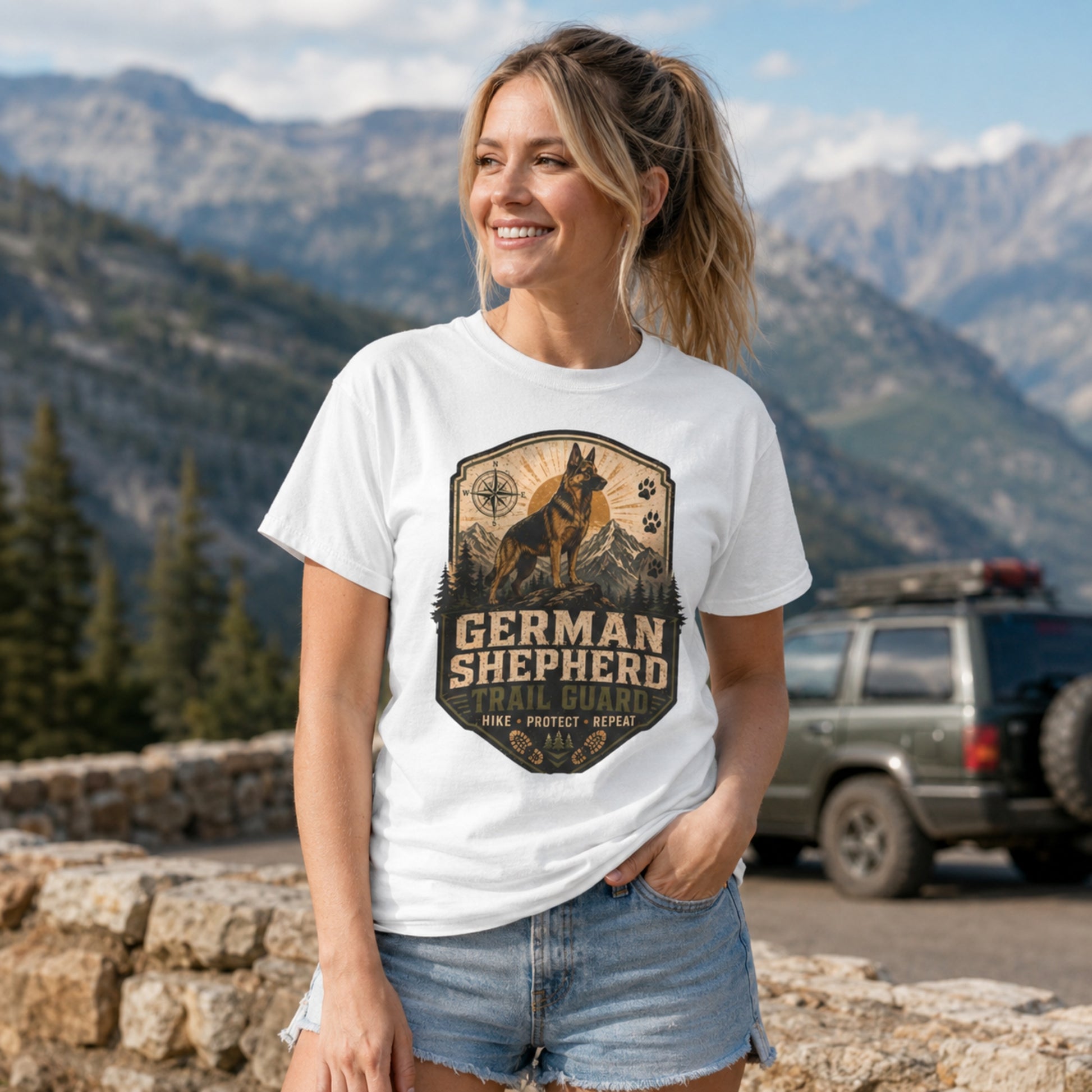 Woman wearing a white German Shepherd Trail Guard T-shirt at a mountain overlook.