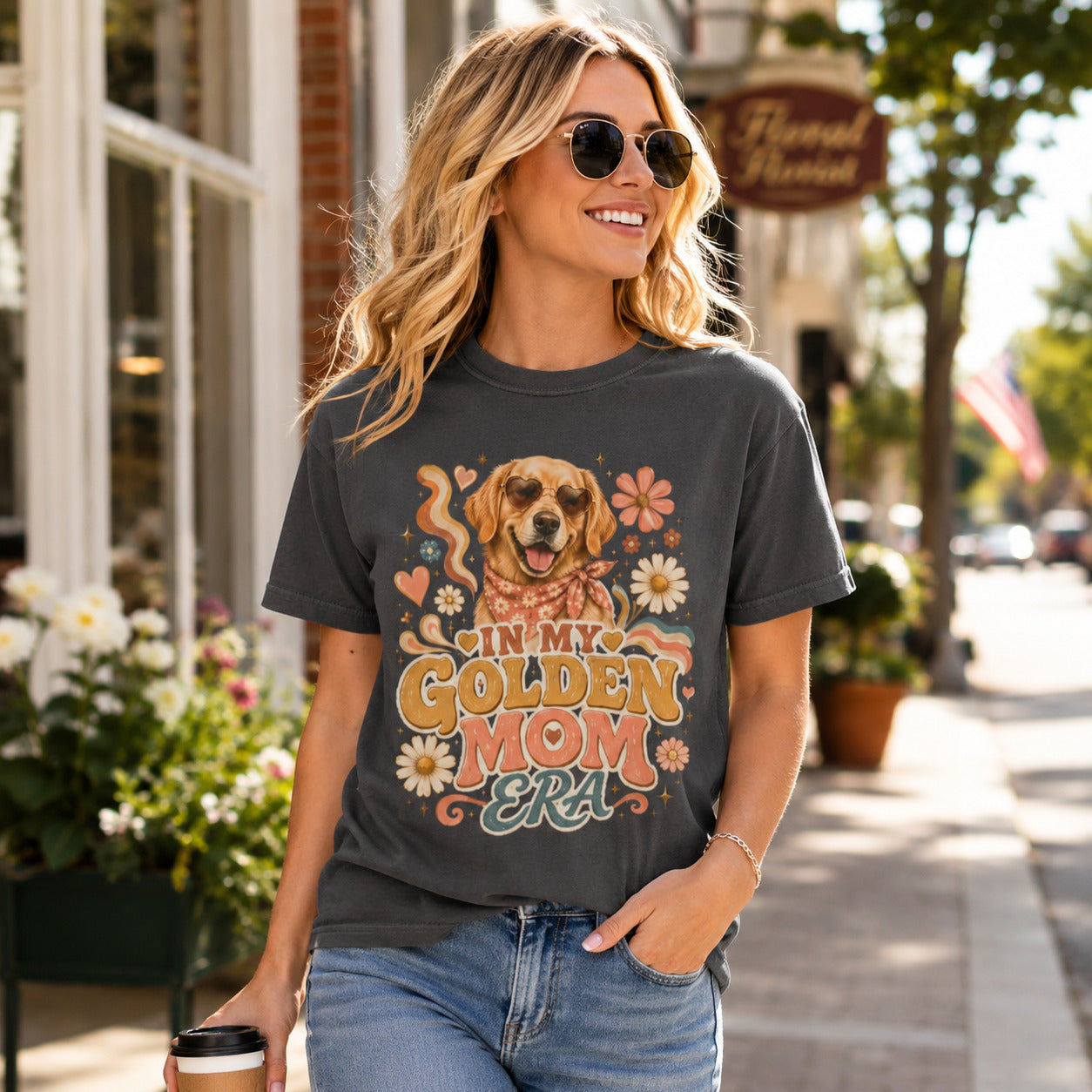 Woman walking a street with sunglasses holding coffee, wearing graphite 'In My Golden Mom Era' retro floral t-shirt