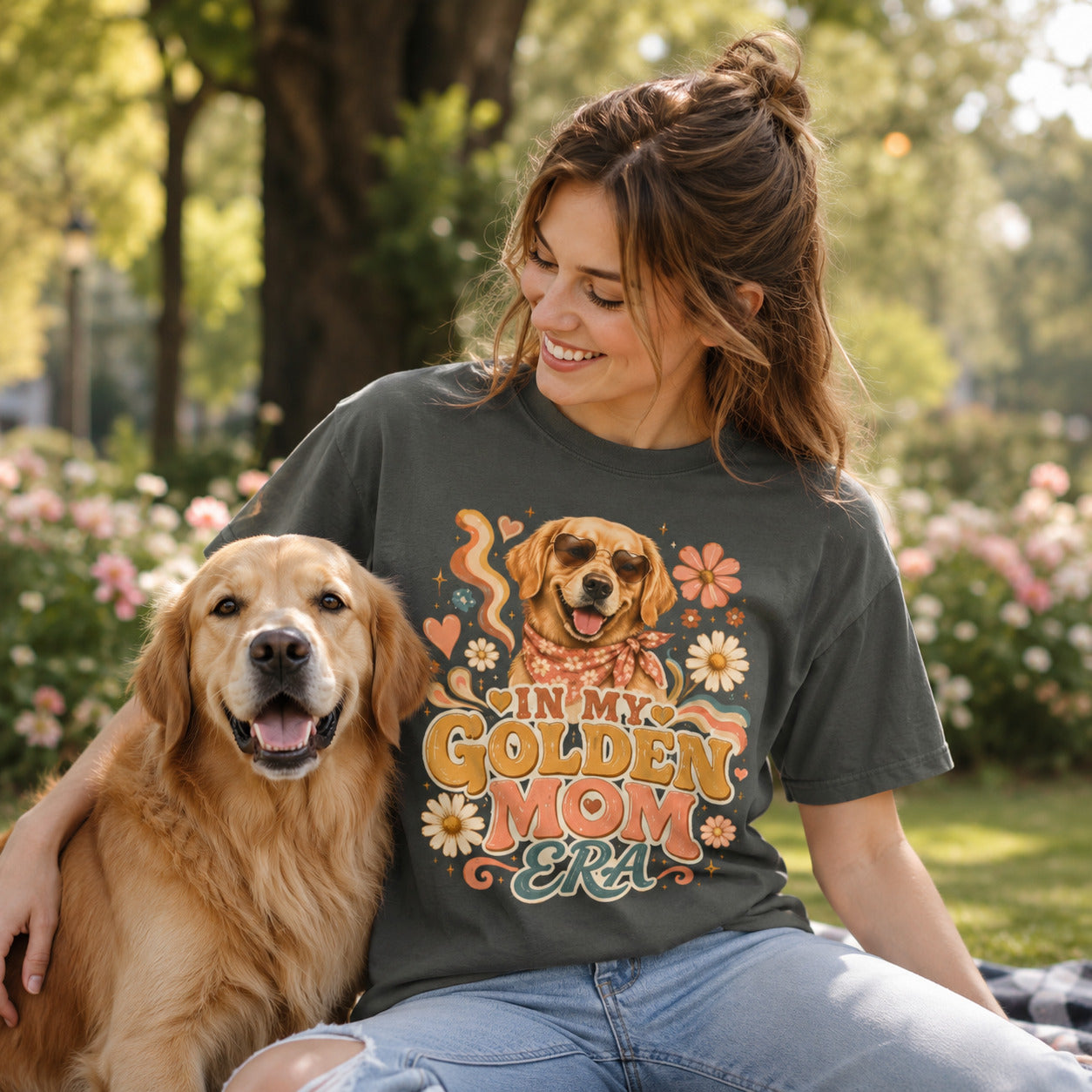 Woman sitting on grass with her golden retriever, wearing pepper 'In My Golden Mom Era' retro floral t-shirt