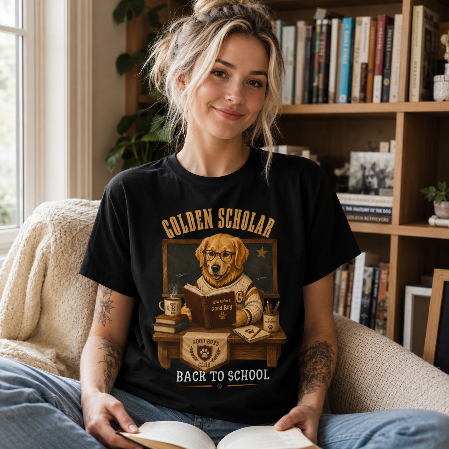 Woman wearing a black Golden Scholar Dog T-shirt in a reading nook with a golden retriever classroom graphic.