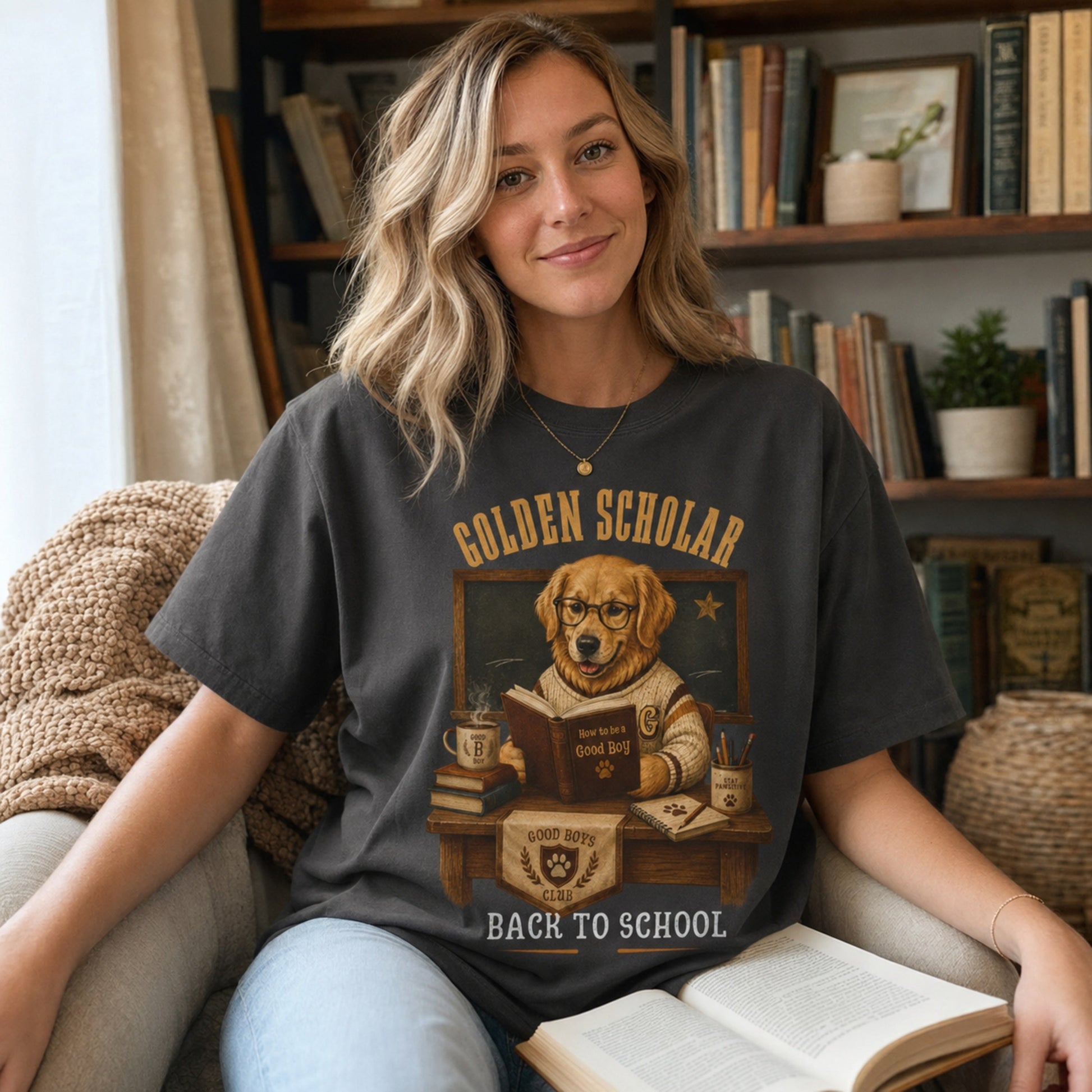 Woman wearing a graphite Golden Scholar Dog T-shirt in a reading nook with a golden retriever classroom graphic.
