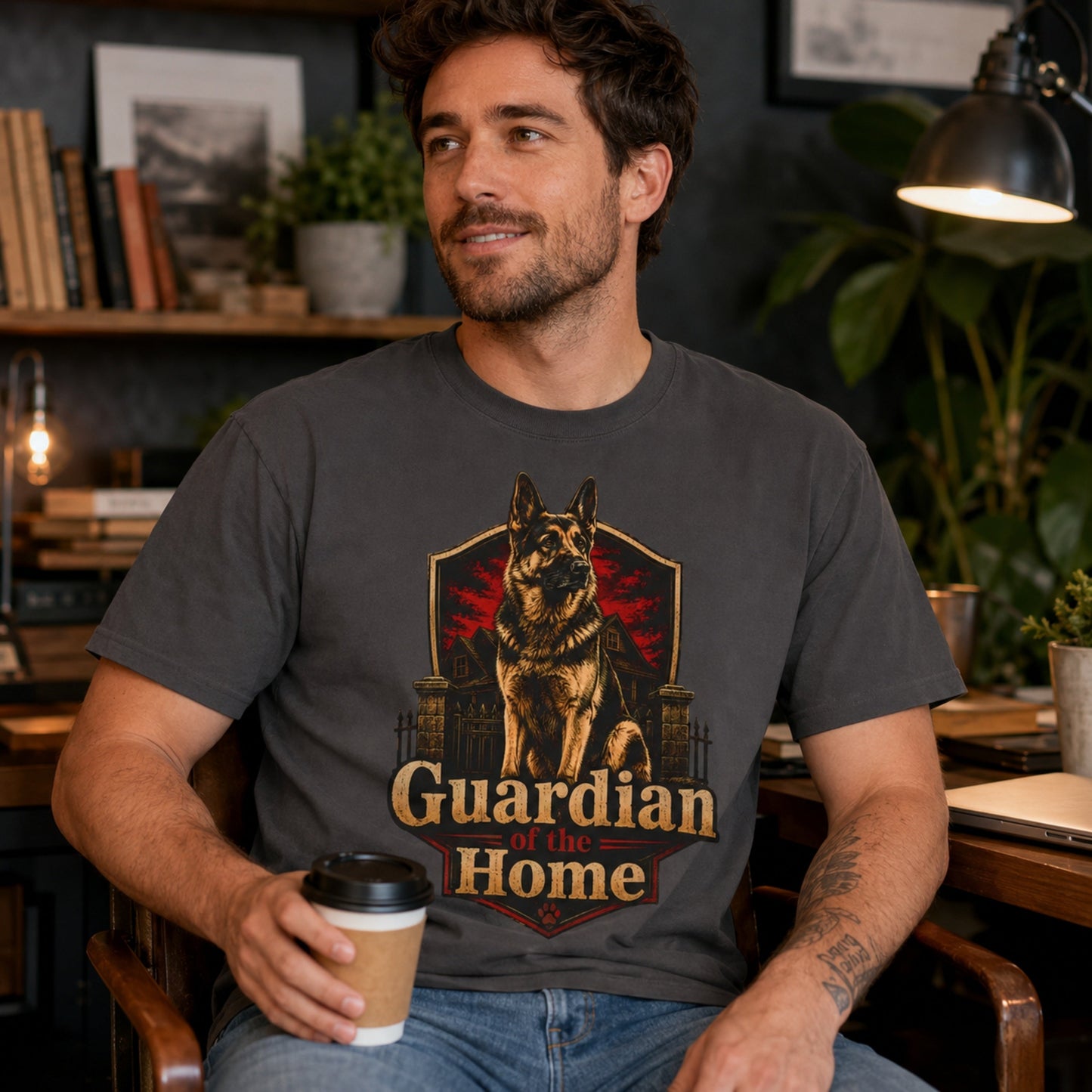 Man wearing a graphite Guardian of the Home German Shepherd T-shirt in a home office while holding coffee.
