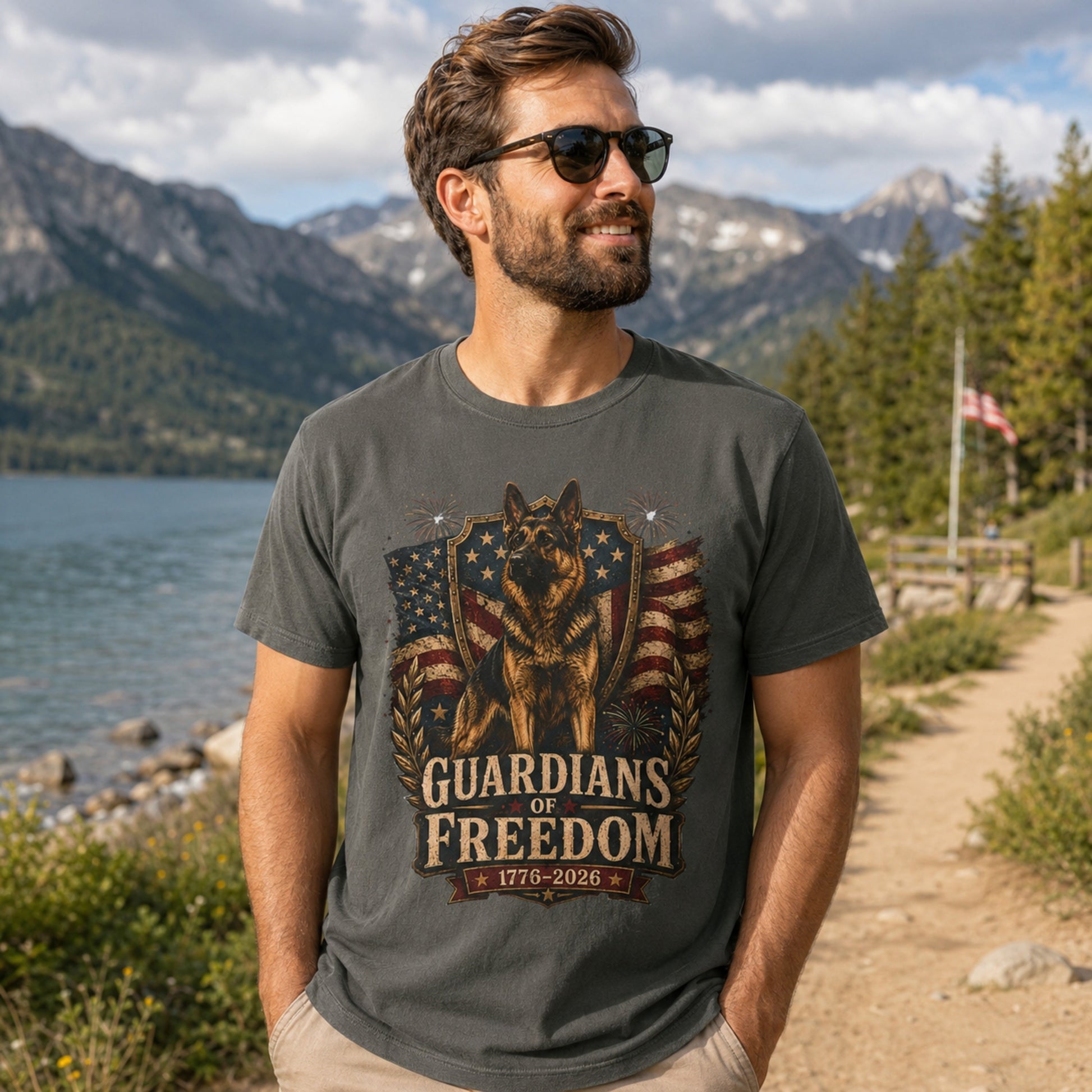 Man wearing a pepper Guardians of Freedom K-9 T-shirt with a German Shepherd patriotic graphic near a mountain lakeside trail.