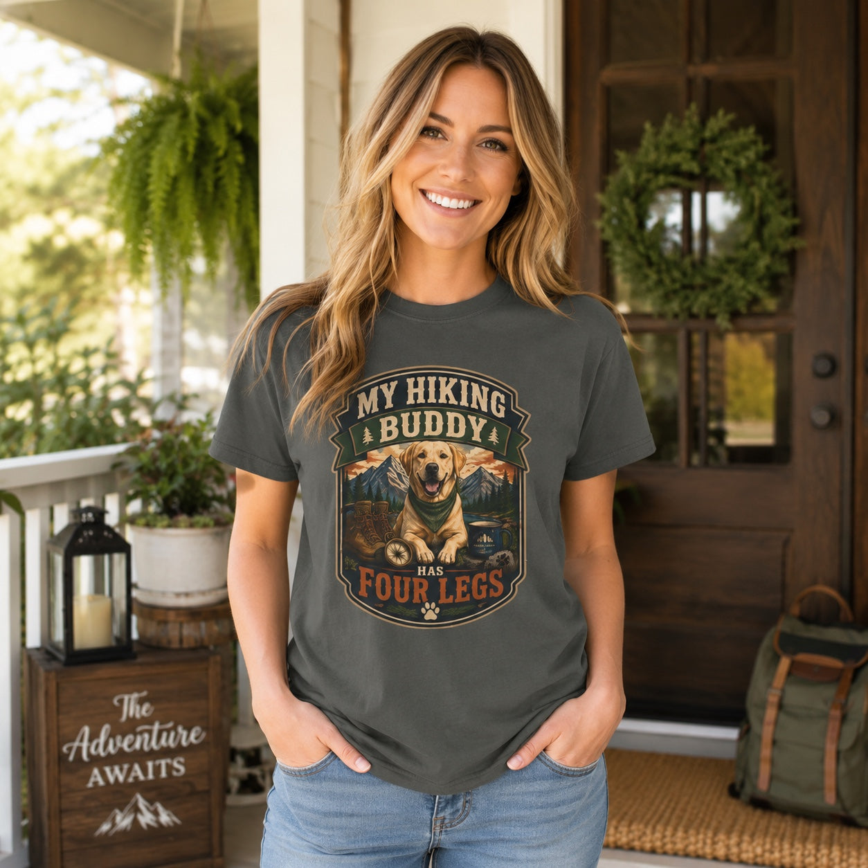 Woman with backpack standing at a porch entryway with an 'Adventure Awaits' sign, wearing pepper 'My Hiking Buddy Has Four Legs' dog t-shirt