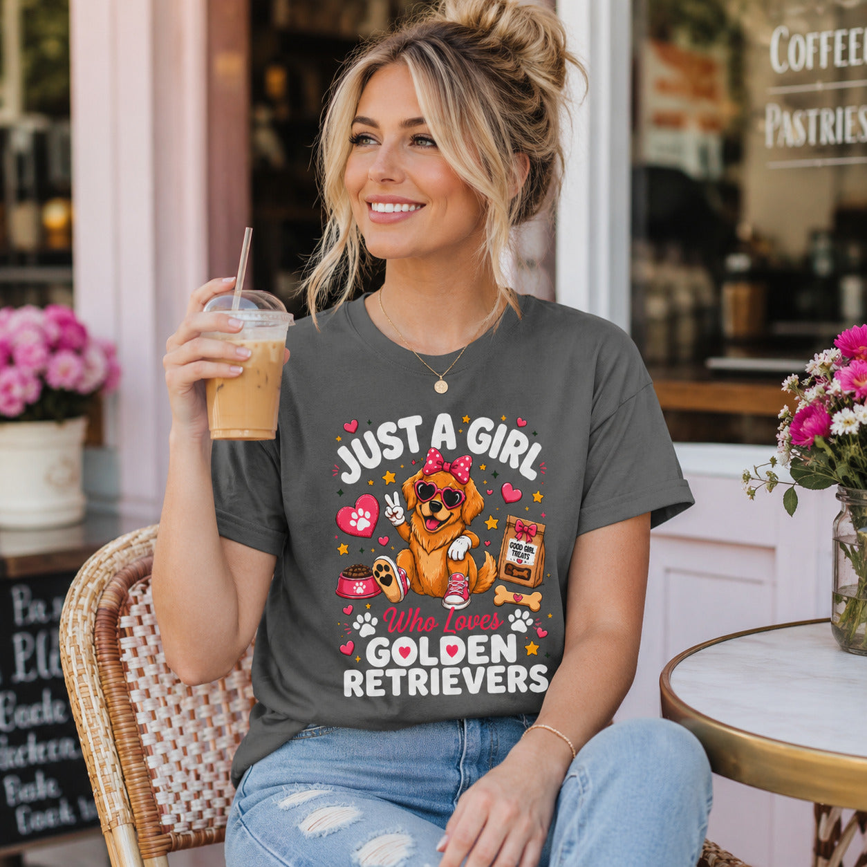 Woman sitting at an outdoor cafe holding iced coffee, wearing pepper 'Just A Girl Who Loves Golden Retrievers' t-shirt