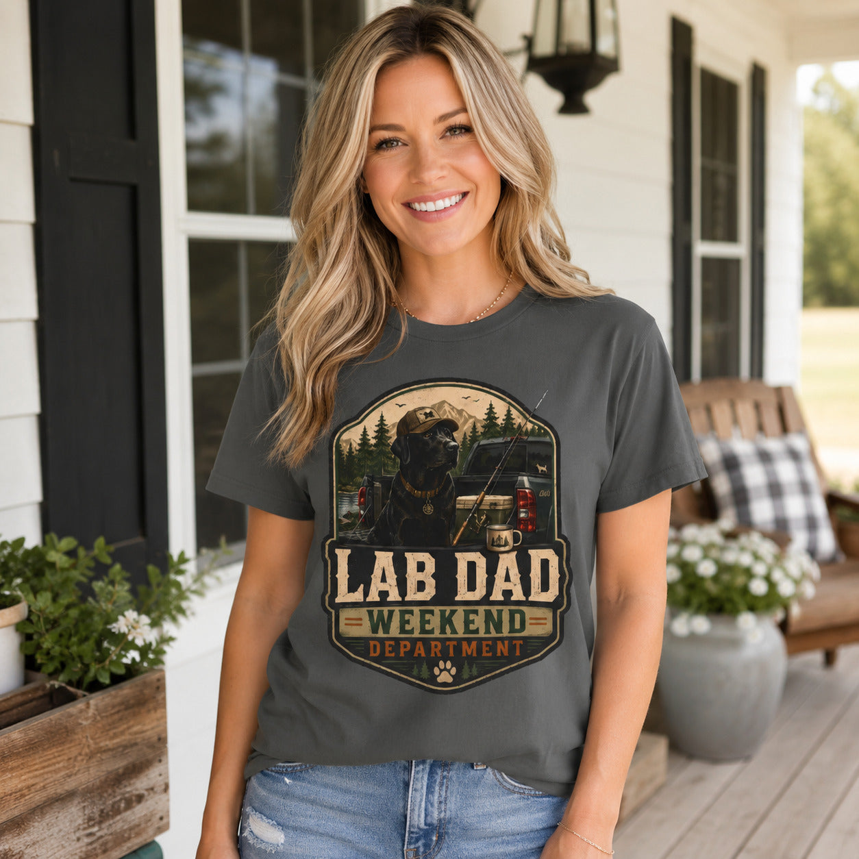 Woman standing on a porch surrounded by flowers, wearing pepper 'Lab Dad Weekend' fishing camping t-shirt