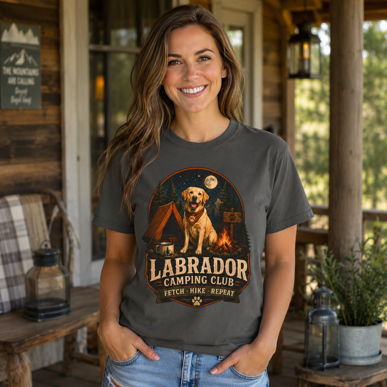 Woman wearing a graphite Labrador Camping Club Fetch Hike Repeat T-shirt on a rustic outdoor porch.