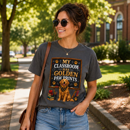 Woman wearing a graphite My Classroom Has Golden Paw Prints T-shirt with a Golden Retriever classroom design while walking outdoors on a school campus with a shoulder bag.