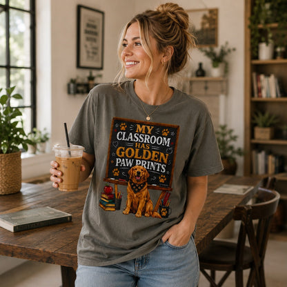 Woman wearing a pepper My Classroom Has Golden Paw Prints T-shirt with a Golden Retriever classroom design while holding iced coffee in an indoor study room.