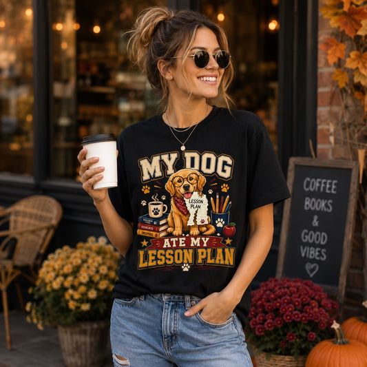 Smiling young woman wearing a black Comfort Colors 1717 T-shirt featuring the “My Dog Ate My Lesson Plan” Golden Retriever teacher design while holding a takeaway coffee outside a café.