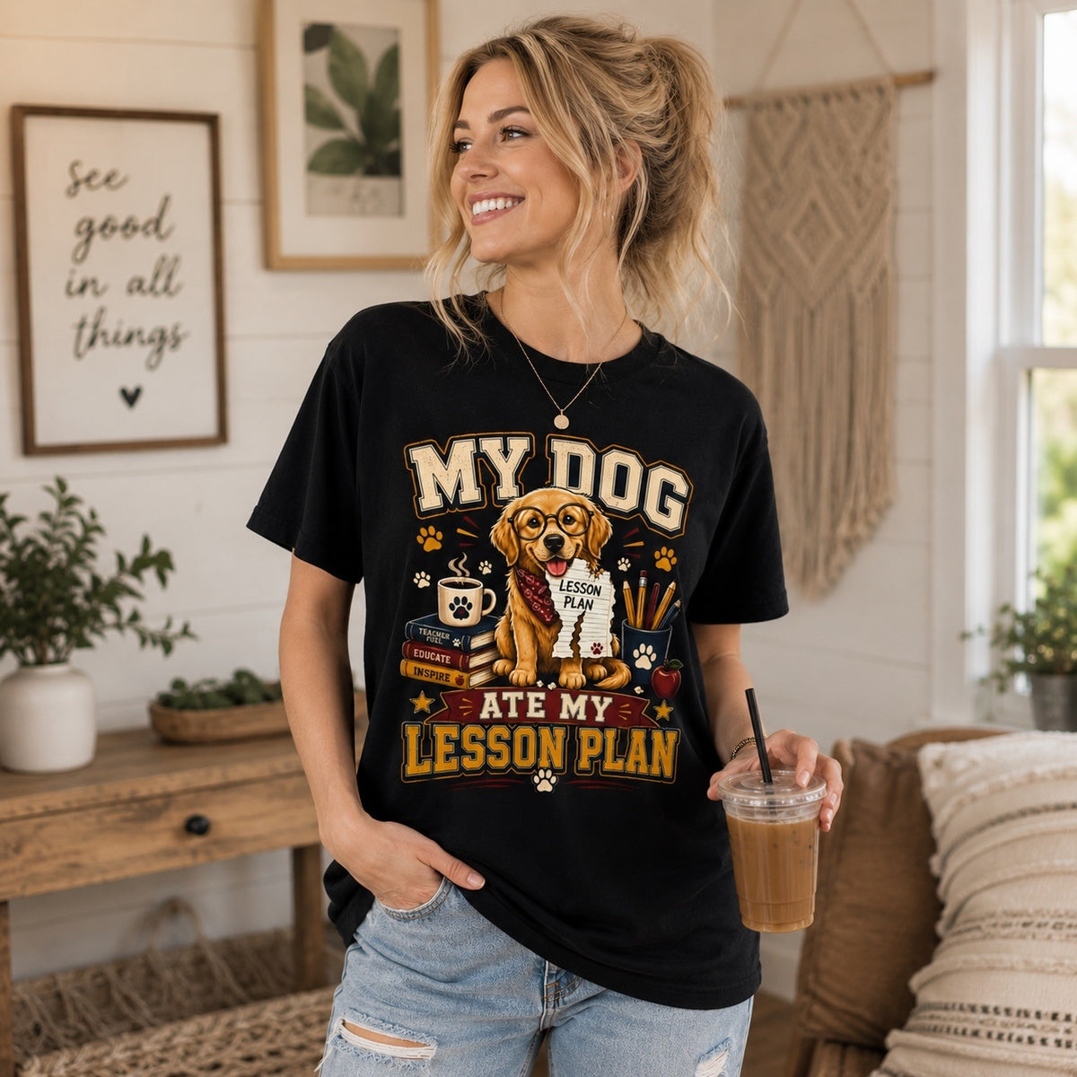Young woman wearing a black “My Dog Ate My Lesson Plan” Golden Retriever teacher T-shirt while holding an iced coffee in a cozy indoor living room, featuring a colorful dog lover graphic with school-themed artwork.