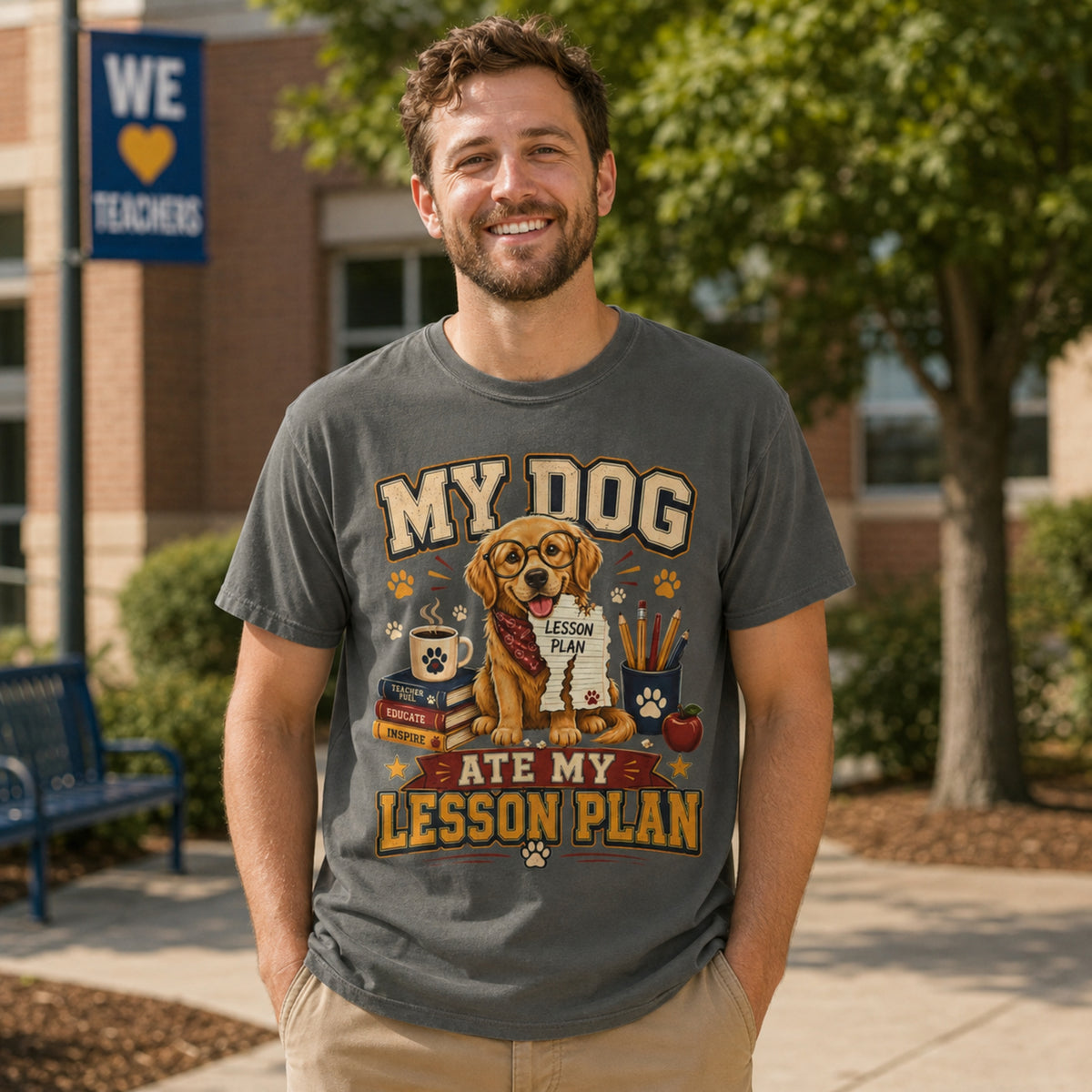 Man wearing a Pepper “My Dog Ate My Lesson Plan” T-shirt outdoors in a school courtyard with golden retriever teacher artwork.