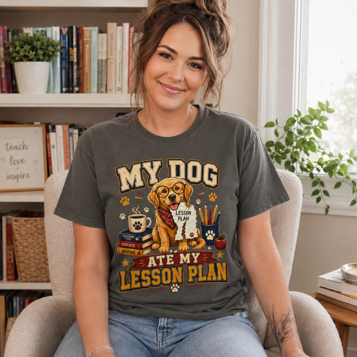 Woman wearing a Pepper “My Dog Ate My Lesson Plan” T-shirt indoors near a bookshelf with golden retriever teacher artwork.