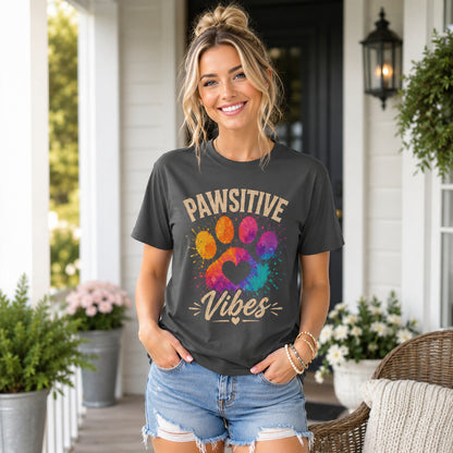 Woman standing on a porch with decor, wearing graphite 'Pawsitive Vibes' colorful paw t-shirt