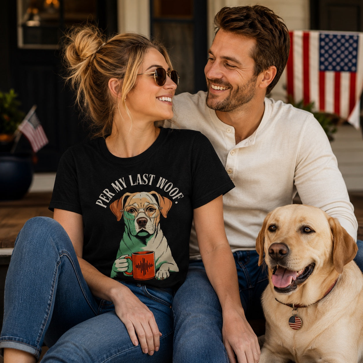 Couple sitting together with their Labrador on a porch with flag decor, wearing black 'Per My Last Woof' t-shirts