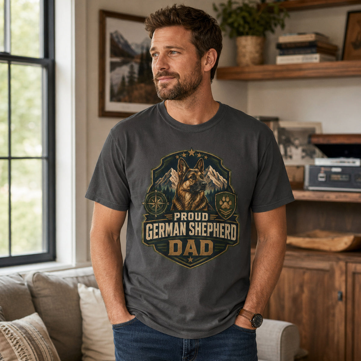 Man wearing a graphite Proud German Shepherd Dad T-shirt in a casual living room.