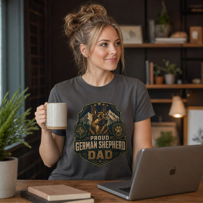 Woman wearing a graphite Proud German Shepherd Dad T-shirt while holding coffee near a laptop.