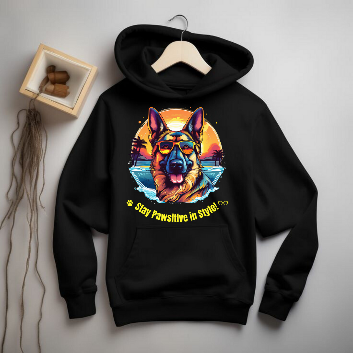 Black Stay Pawsitive in Style hoodie with a German Shepherd graphic displayed on a hanger against a light wall.