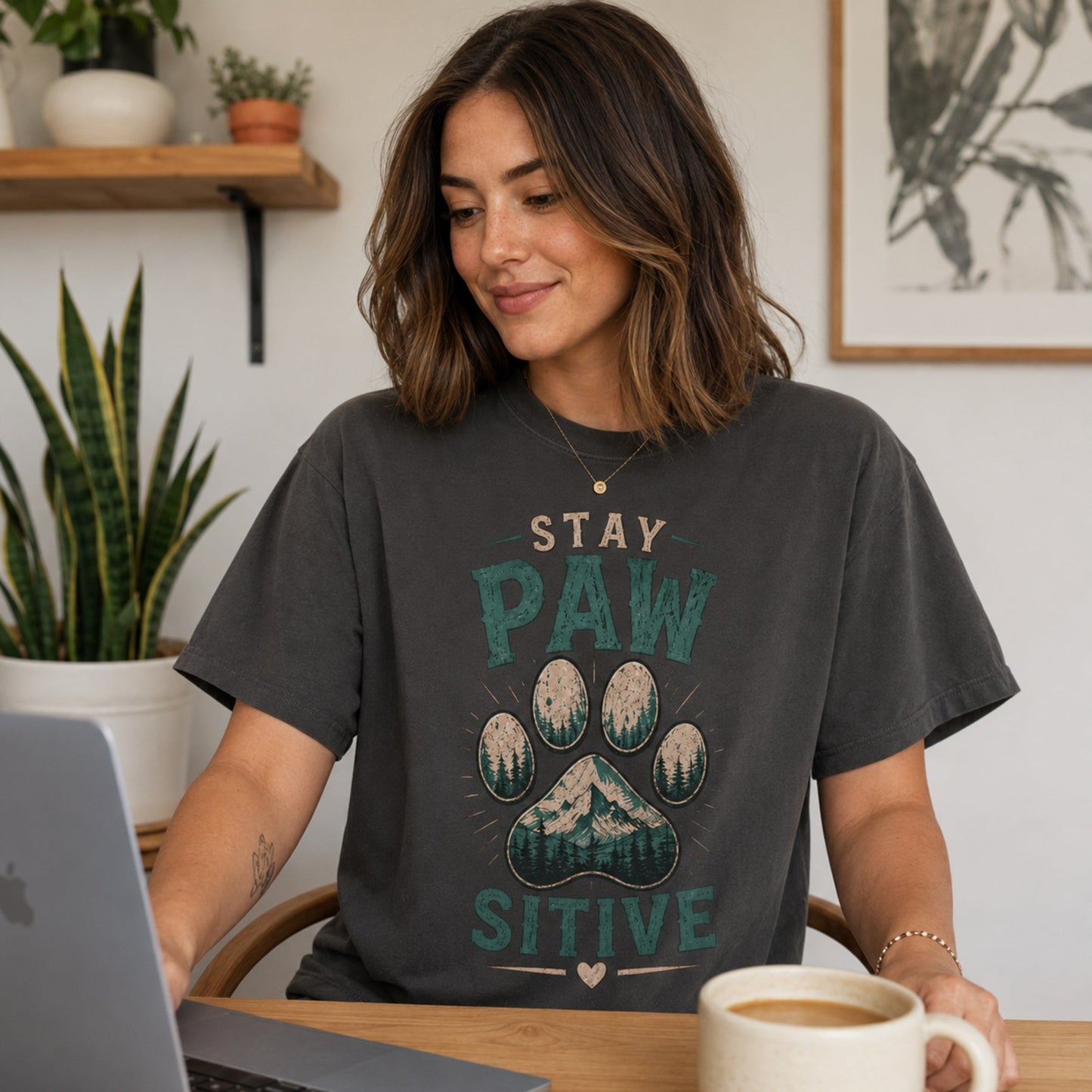Woman wearing a graphite Stay Pawsitive T-shirt at a desk with a laptop and coffee mug.