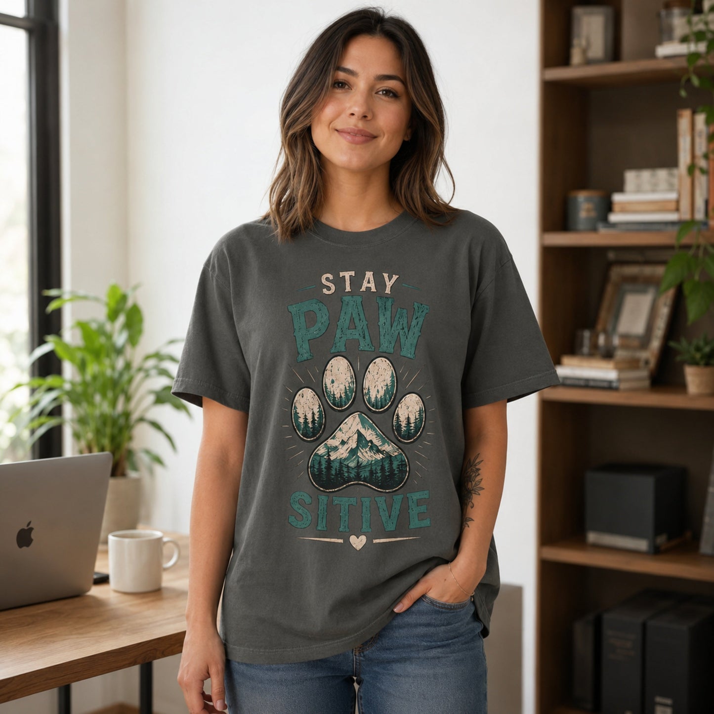 Woman wearing a pepper Stay Pawsitive T-shirt in a workspace with a laptop and coffee mug.