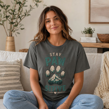 Woman wearing a pepper Stay Pawsitive T-shirt while sitting on a sofa in a living room.