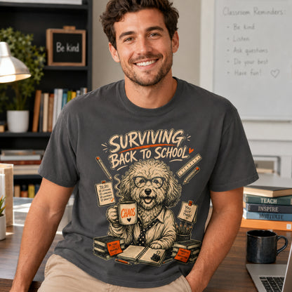 Man wearing a graphite Surviving Back to School dog teacher T-shirt with coffee, books, and a laptop.