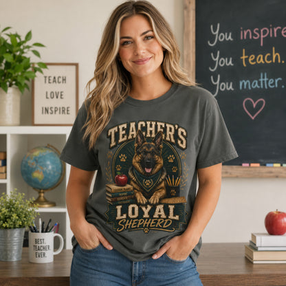 Woman wearing a pepper Teacher’s Loyal Shepherd T-shirt with a German Shepherd graphic in a classroom lifestyle scene.