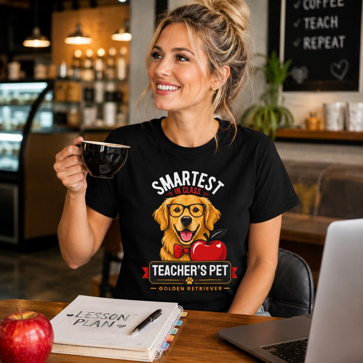 Woman holding coffee at her desk with a laptop, wearing black 'Teacher's Pet Golden Retriever' t-shirt